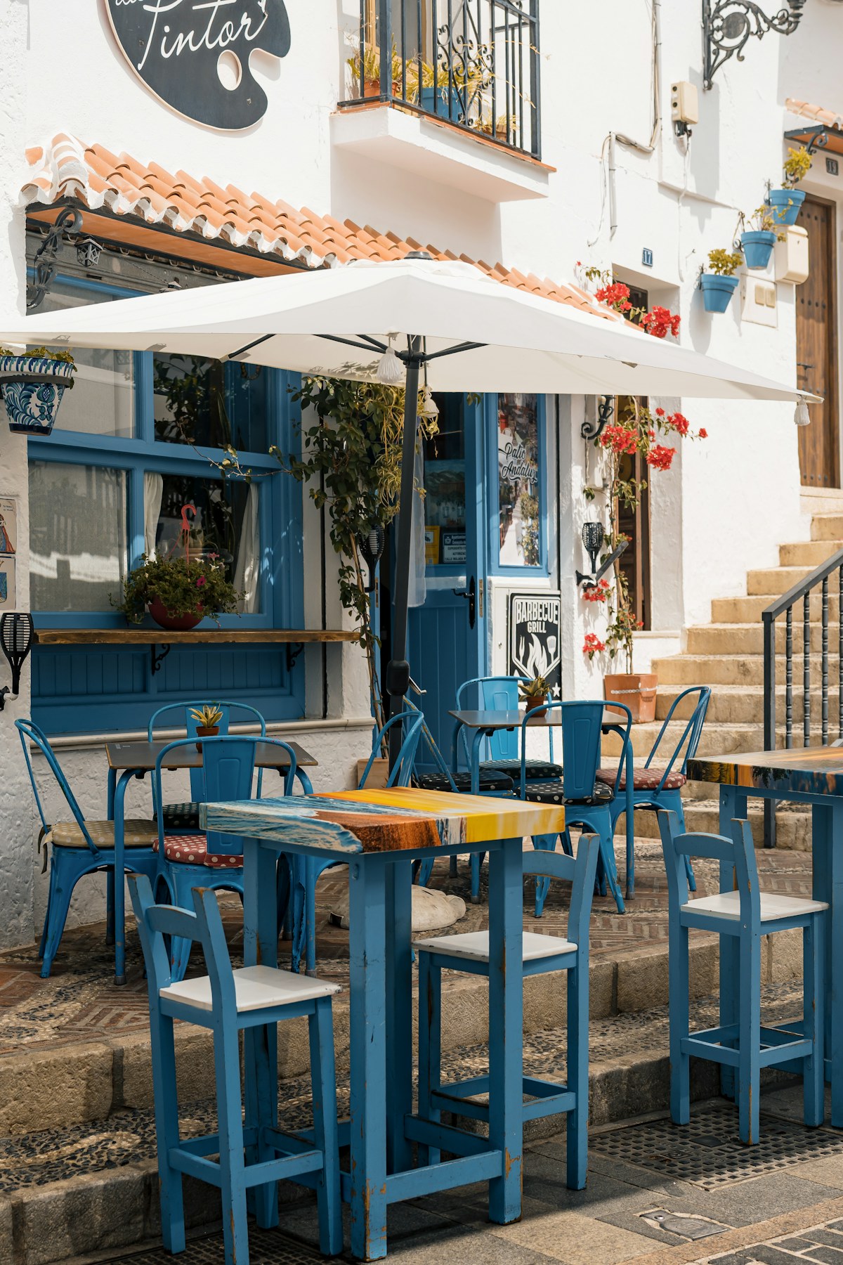 Mediterraan restaurantterras met blauwe stoelen, bloemen en parasols